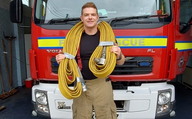 Firefighter in front of fire engine with fire hose over his shoulders