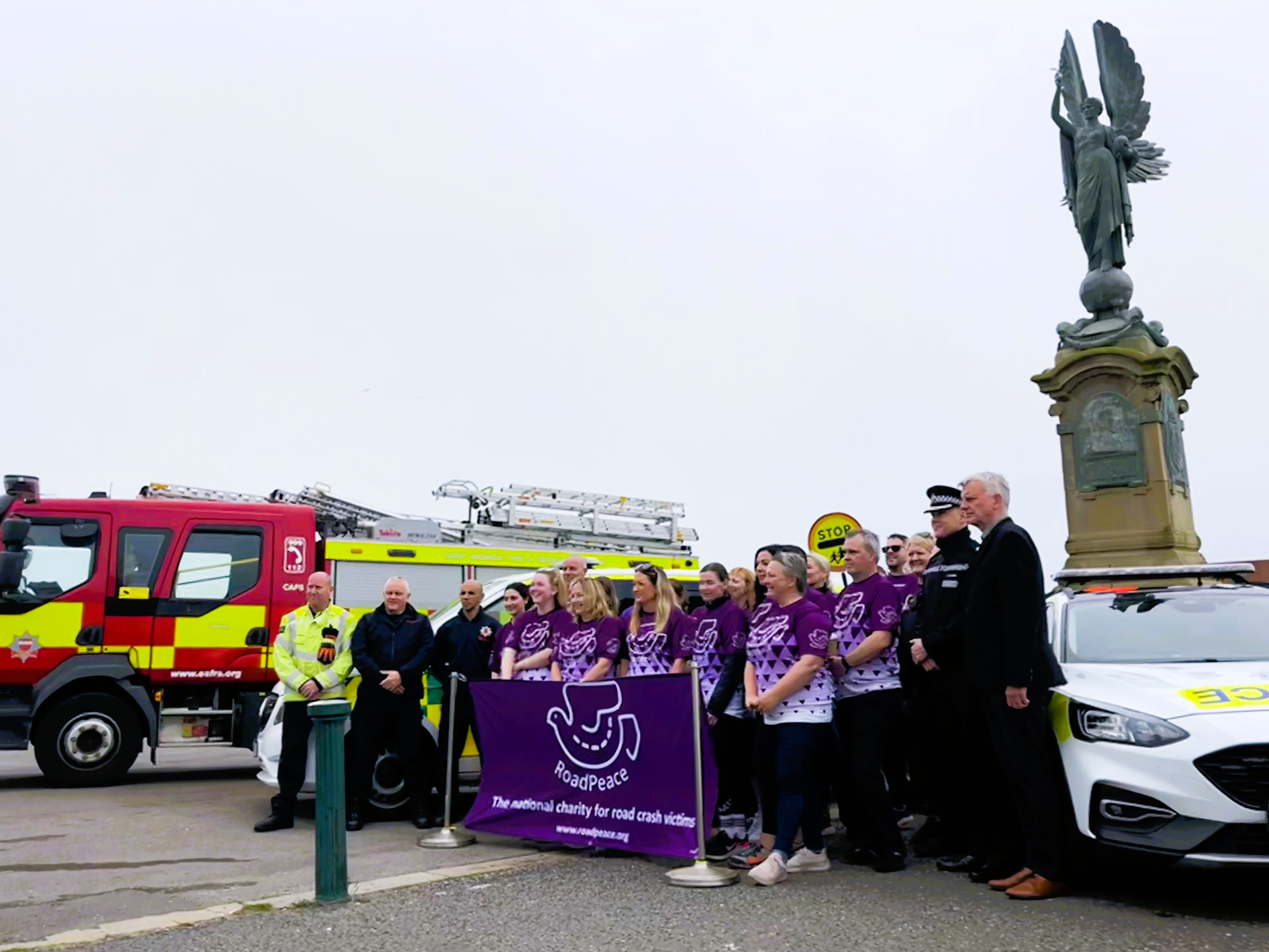 Crowd gathered in front of Hove Peace statue with emergency vehicles and RoadPeace banner
