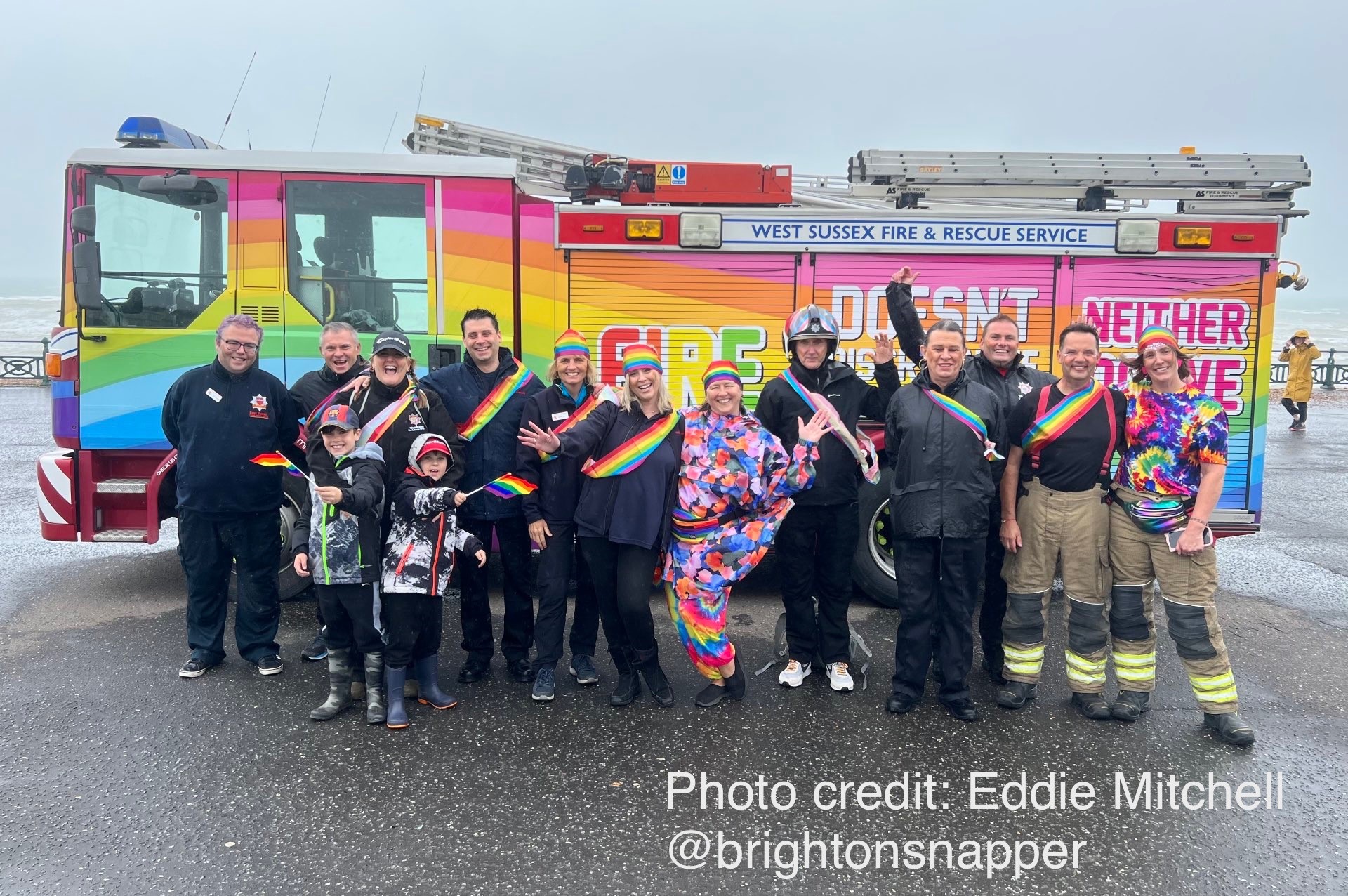 Photo of a group of people standing in front of rainbow coloured Fire engine celebrating Pride
