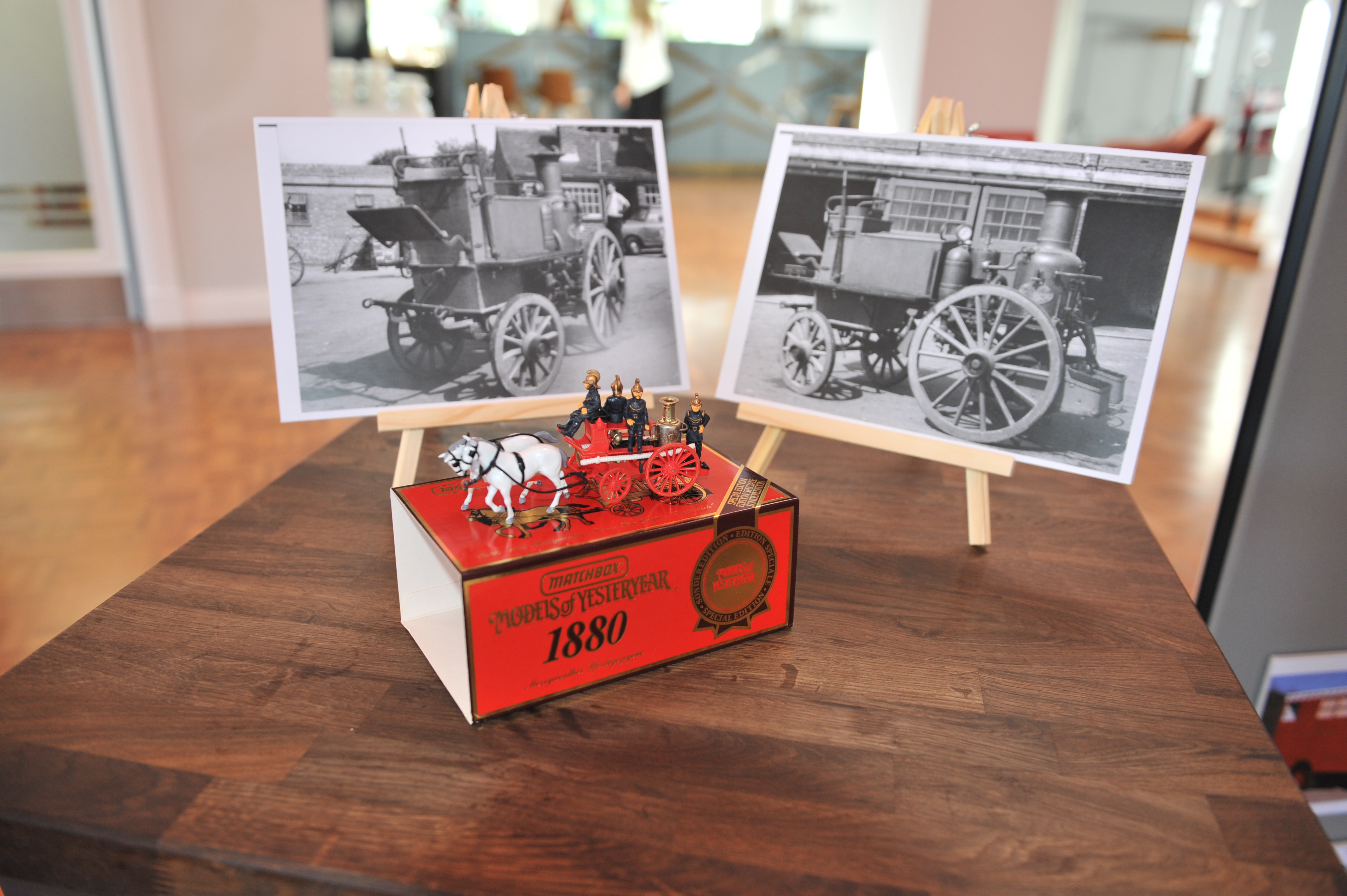 Photo of red matchbox replica of Merryweather fire engine with two black and white photos of the Merryweather in the background