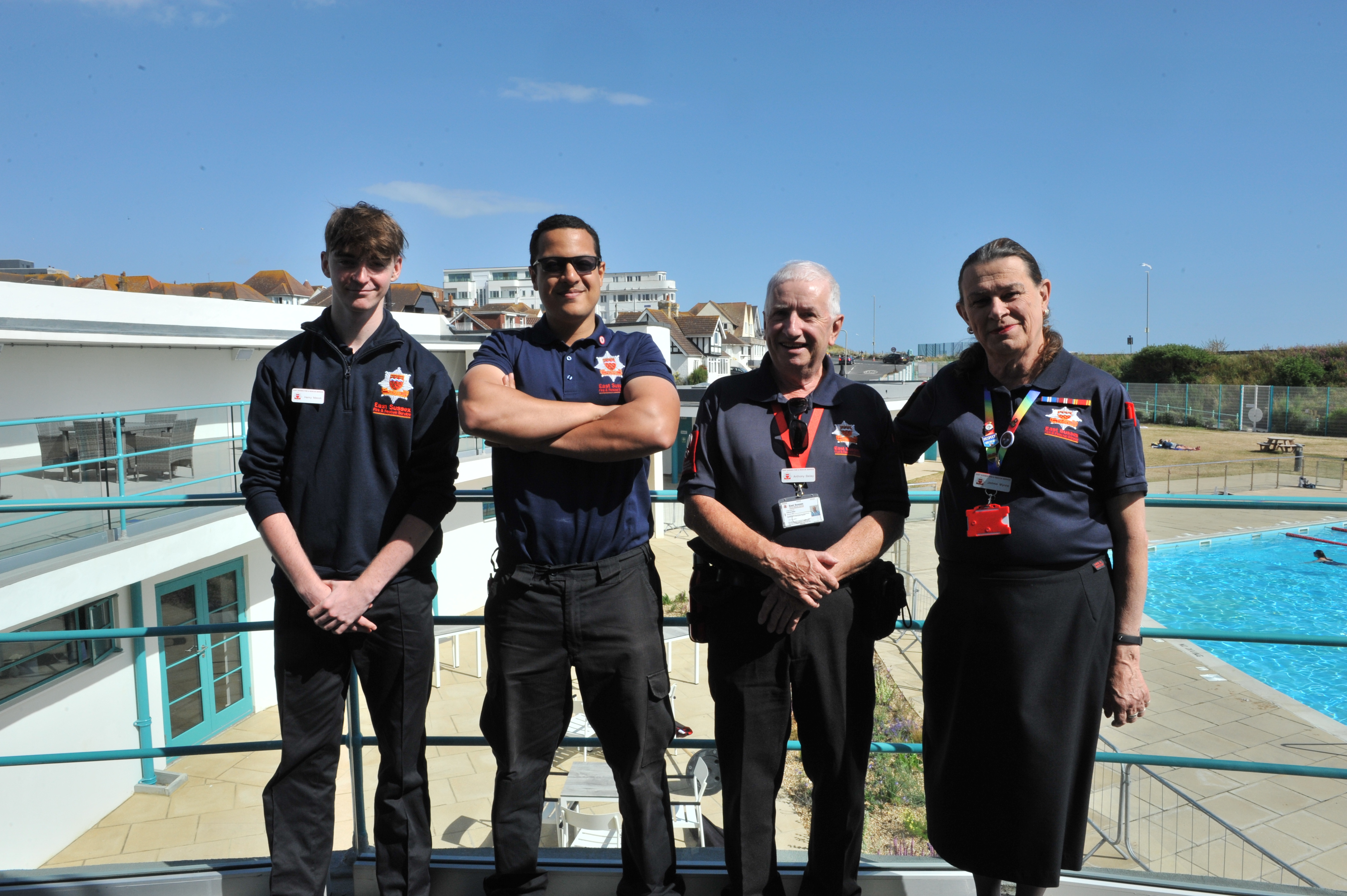 Photo of four community volunteers at Saltdean Lido event. Standing on balcony with blue sky and blue Lido in the background