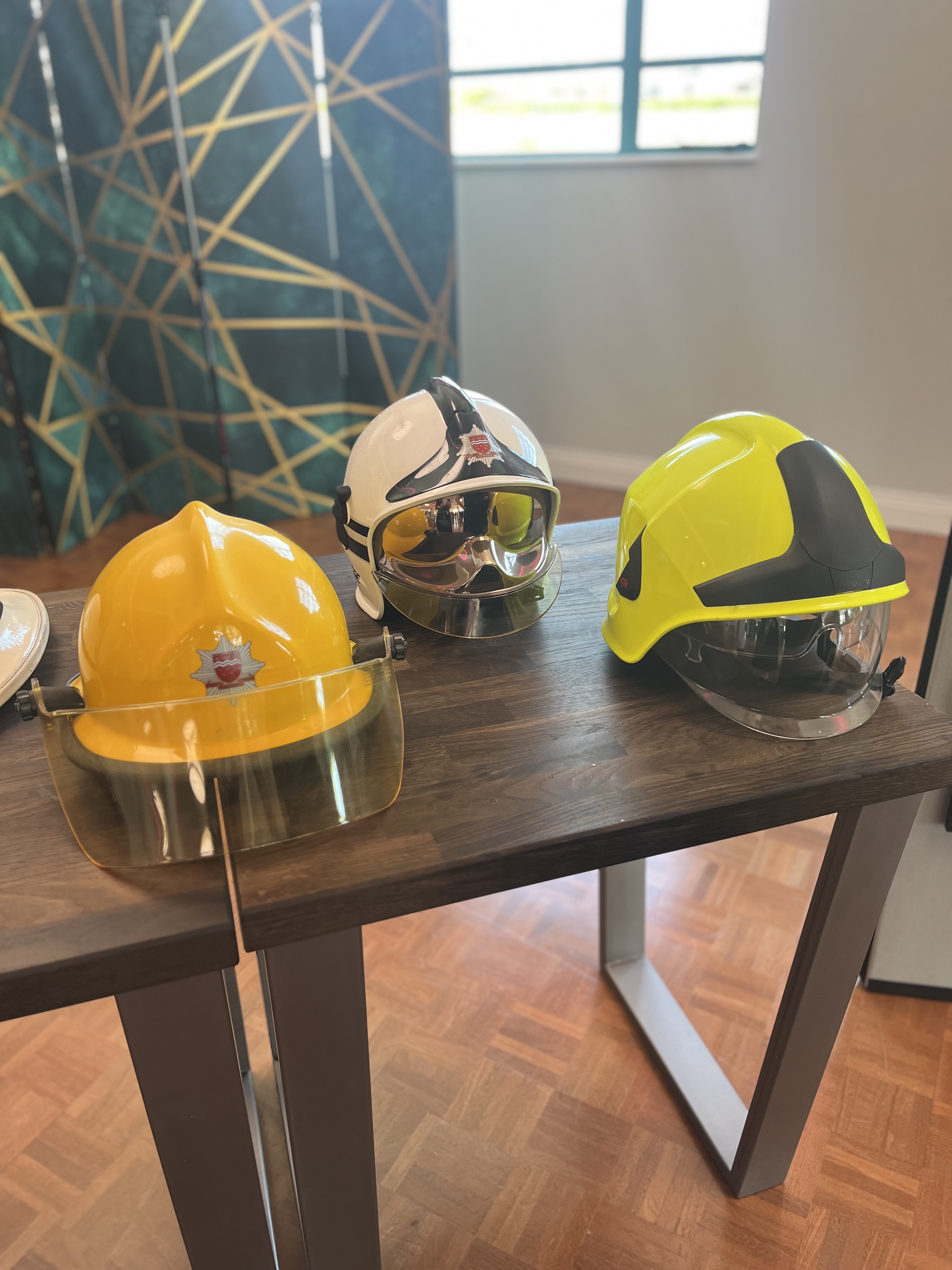Three more recent fire helmets in yellow white and hi viz on display on wooden table