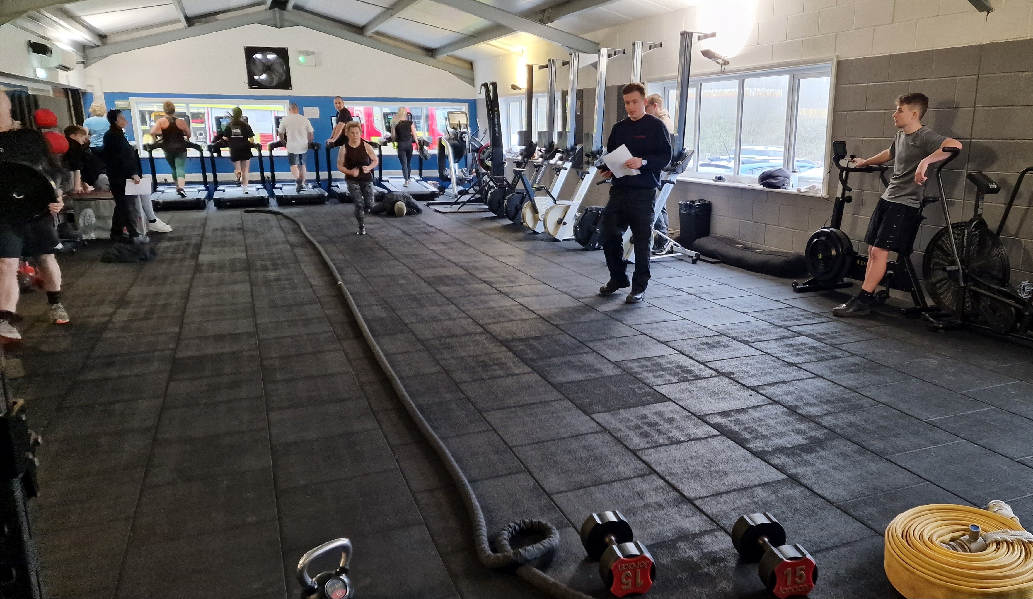 Photo of gym with people on treadmills and one person running with one trainer for firefighter recruitment event