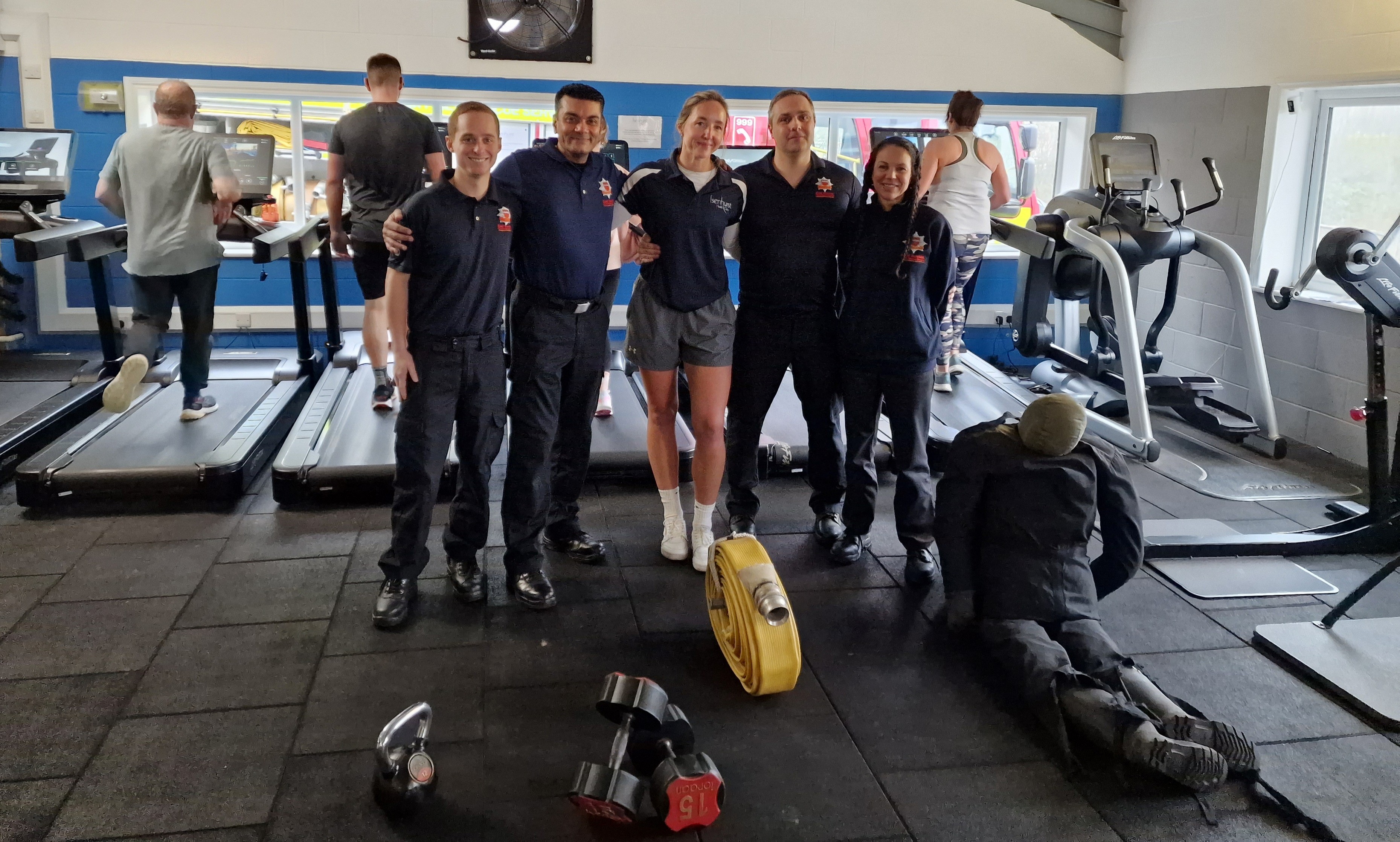 Photo of five people posing for a photo in a gym at a firefighter recruitment event