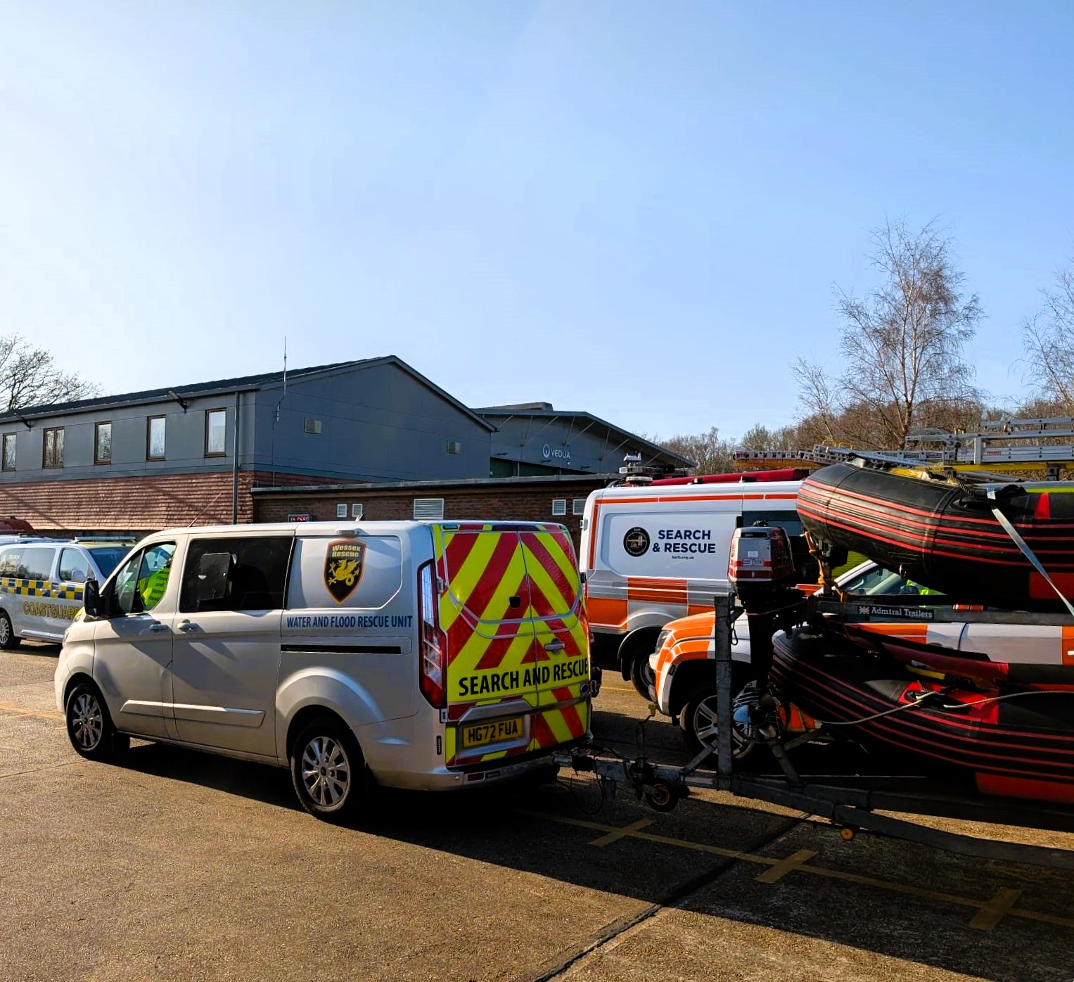 Coastguard and search and rescue vans and dinghy in a yard on a sunny day,