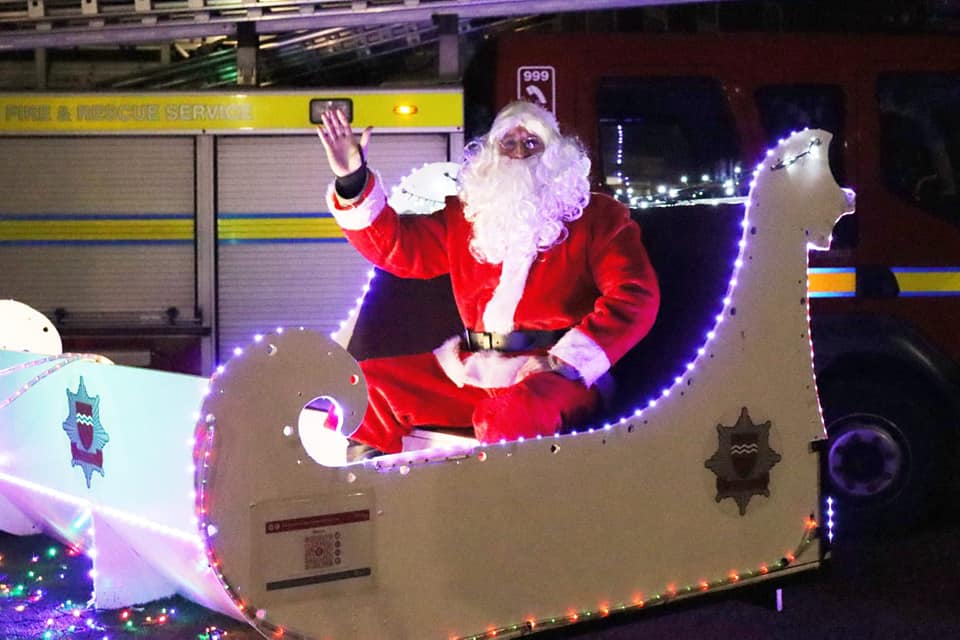 Santa sitting on white sleigh in front of fire engine. Sleigh has lights around it and East Sussex Fire and Rescue Service crest
