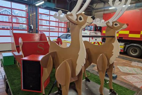 Two wooden reindeers in front of a red sleigh in a fire appliance bay.