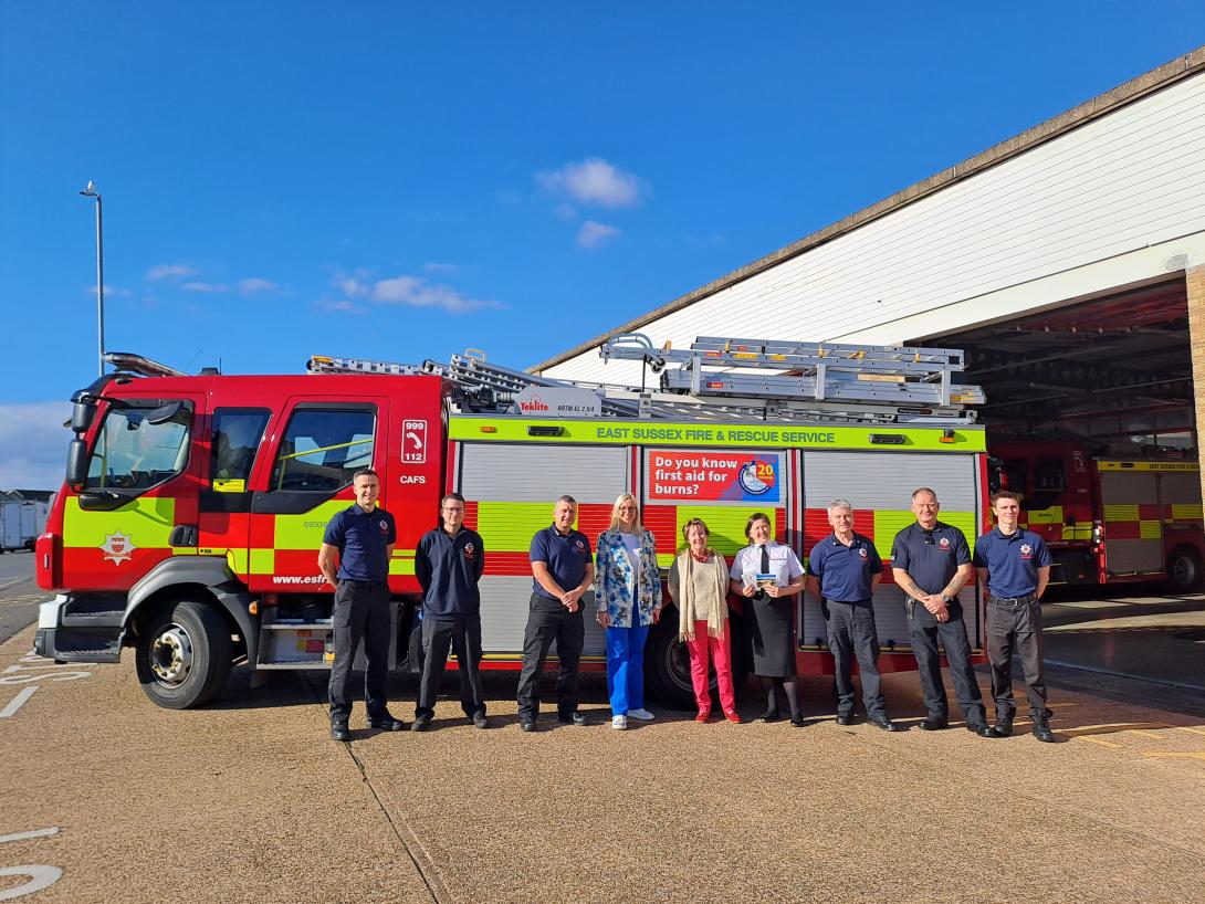 Photo of fire engine with fire crew and Burns Trust members posing with burns first aid sticker on appliance