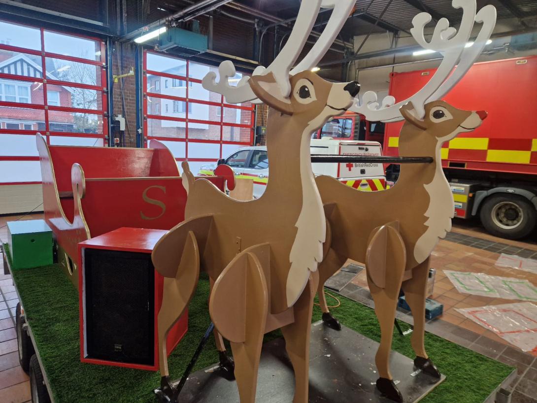 Two wooden reindeers in front of a red sleigh in a fire appliance bay.